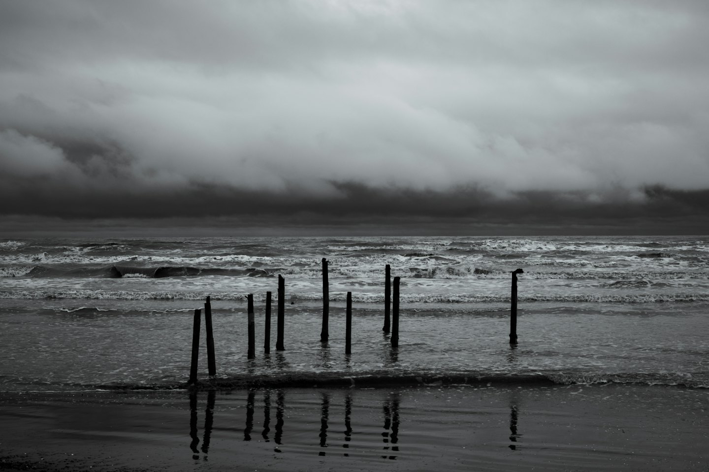 Waves crash against wooden posts on a wet sandy beach.