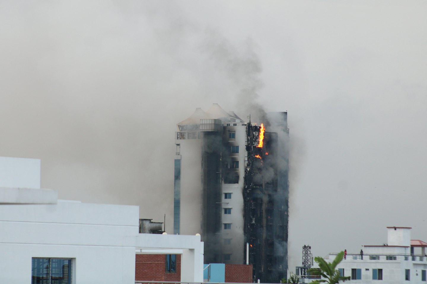 A modern skyscraper burning with thick smoke rising into the sky.